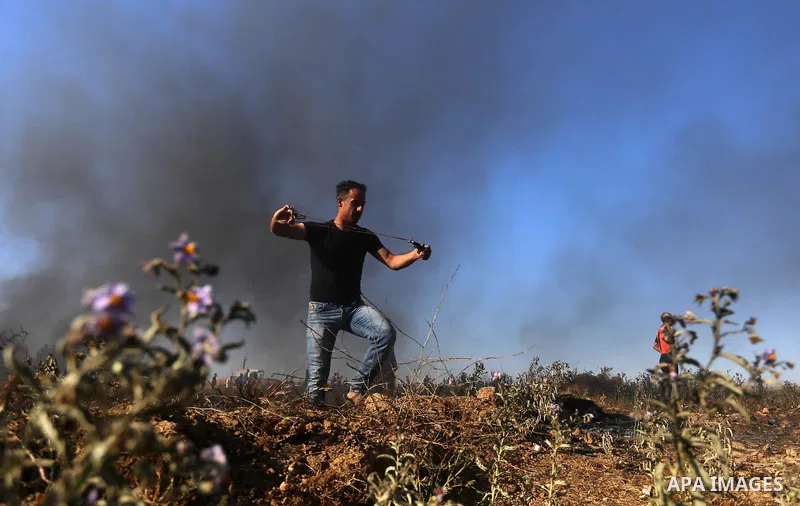 A Palestinian protester uses a slingshot to hurl stones towards Israeli security forces during clashes following a demonstration against the blockade on the Gaza Strip, near the border fence east of Jabalia refugee camp...