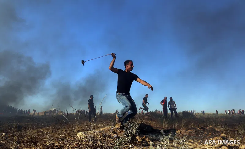 A Palestinian protester uses a slingshot to hurl stones towards Israeli security forces during clashes following a demonstration against the blockade on the Gaza Strip, near the border fence east of Jabalia refugee camp...