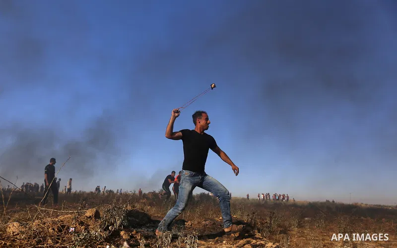A Palestinian protester uses a slingshot to hurl stones towards Israeli security forces during clashes following a demonstration against the blockade on the Gaza Strip, near the border fence east of Jabalia refugee camp...