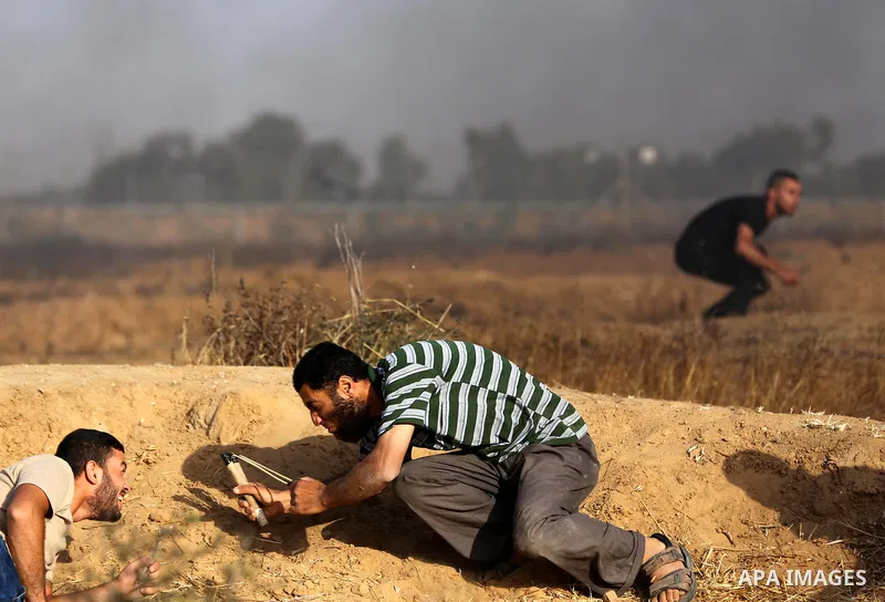 A Palestinian protester uses a slingshot to hurl stones towards Israeli security forces during clashes following a demonstration against the blockade on the Gaza Strip, near the border fence east of Jabalia refugee camp...