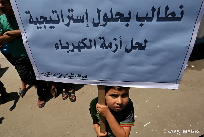 A Palestinian boy holds placards during a protest against power cut in front of the high commissioner for human rights headquarters in Gaza city on June 13, 2017. Photo by Ashraf Amra