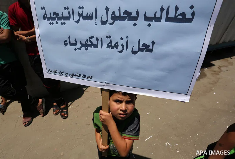 A Palestinian boy holds placards during a protest against power cut in front of the high commissioner for human rights headquarters in Gaza city on June 13, 2017. Photo by Ashraf Amra