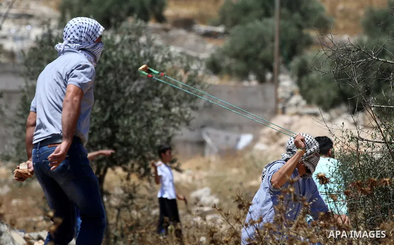 A Palestinian protester uses a slingshot to hurl stones towards Israeli security forces during clashes following a demonstration against the expropriation of Palestinian land by Israel in the village of Kfar Qaddum, near...