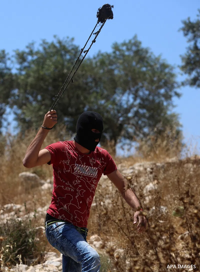A Palestinian protester uses a slingshot to hurl stones towards Israeli security forces during clashes following a demonstration against the expropriation of Palestinian land by Israel in the village of Kfar Qaddum, near...