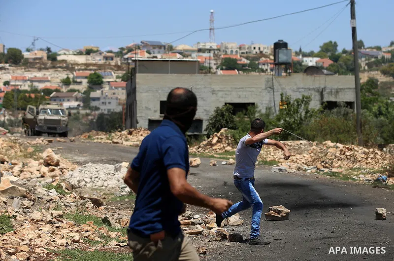 A Palestinian protester uses a slingshot to hurl stones towards Israeli security forces during clashes following a demonstration against the expropriation of Palestinian land by Israel in the village of Kfar Qaddum, near...
