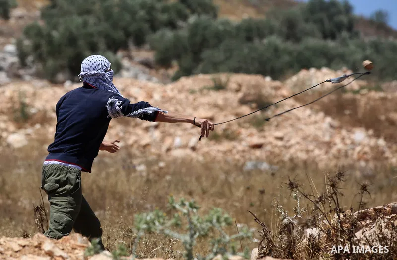 A Palestinian protester uses a slingshot to hurl stones towards Israeli security forces during clashes following a demonstration against the expropriation of Palestinian land by Israel in the village of Kfar Qaddum, near...