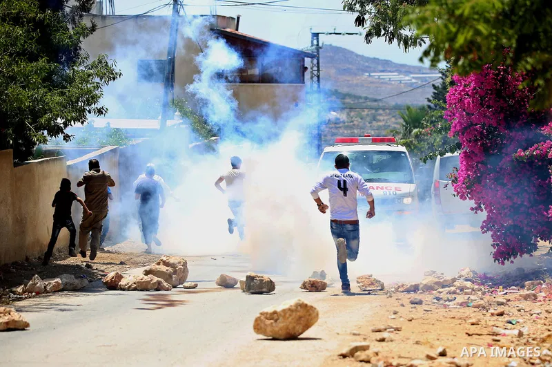 Palestinian protesters run for a cover from a tear gas canister fired by Israeli security forces during clashes following a demonstration against the expropriation of Palestinian land by Israel in the village of Kfar Qad...
