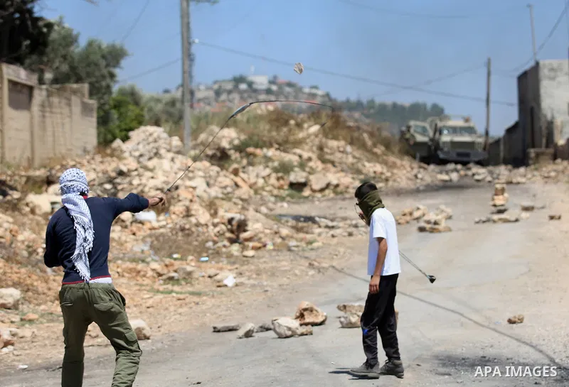 A Palestinian protester uses a slingshot to hurl stones towards Israeli security forces during clashes following a demonstration against the expropriation of Palestinian land by Israel in the village of Kfar Qaddum, near...