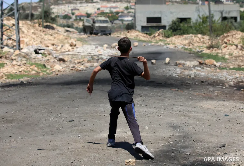 A Palestinian protester uses a slingshot to hurl stones towards Israeli security forces during clashes following a demonstration against the expropriation of Palestinian land by Israel in the village of Kfar Qaddum, near...
