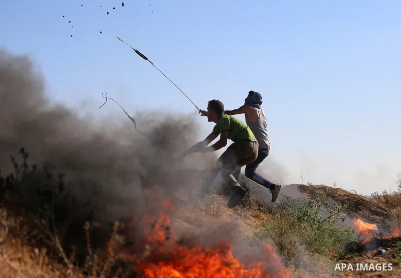 A Palestinian protester uses a slingshot to hurl stones towards Israeli security forces during clashes following a demonstration against the blockade on the Gaza Strip, near the border fence east of Jabalia refugee camp...