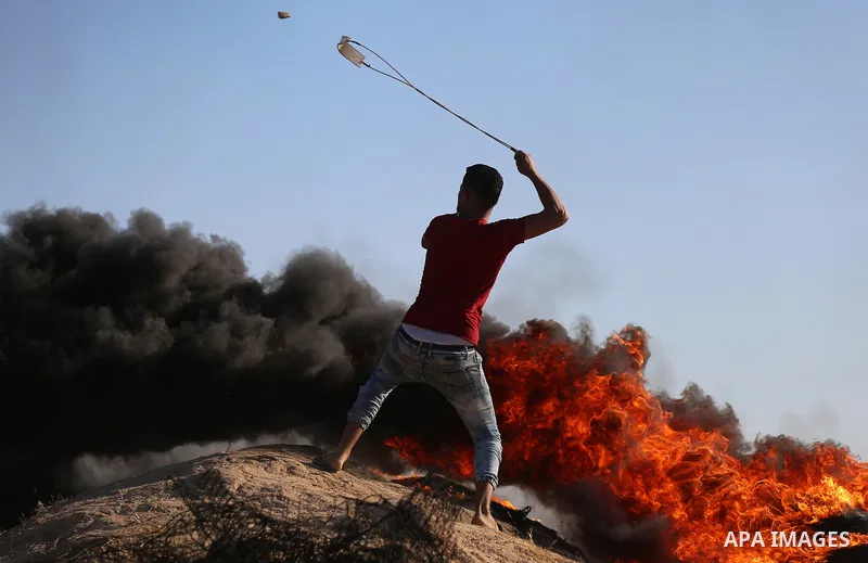 A Palestinian protester uses a slingshot to hurl stones towards Israeli security forces during clashes following a demonstration against the blockade on the Gaza Strip, near the border fence east of Jabalia refugee camp...