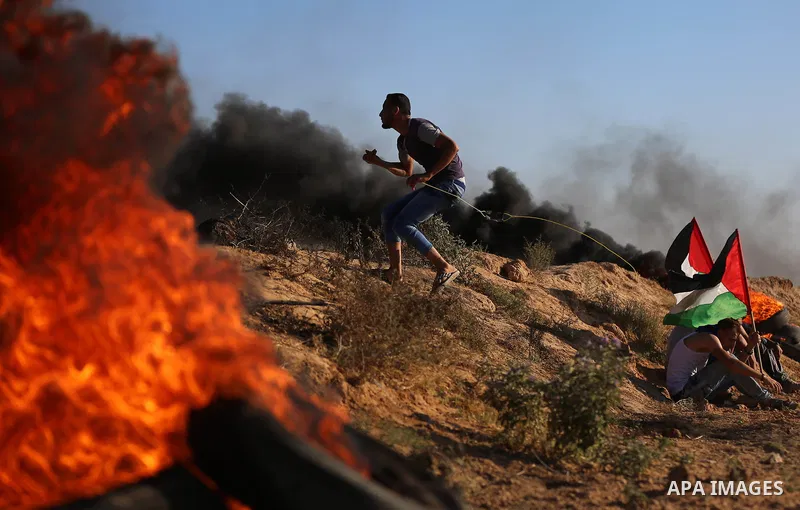 A Palestinian protester uses a slingshot to hurl stones towards Israeli security forces during clashes following a demonstration against the blockade on the Gaza Strip, near the border fence east of Jabalia refugee camp...
