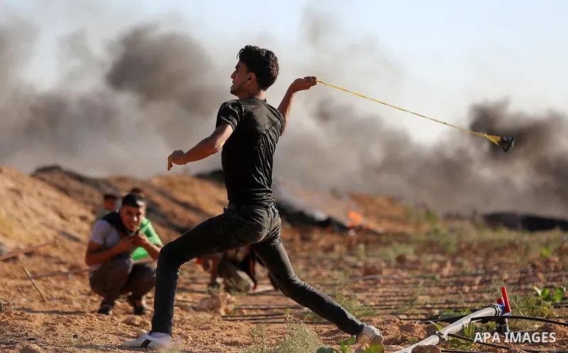 A Palestinian protester uses a slingshot to hurl stones towards Israeli security forces during clashes following a demonstration against the blockade on the Gaza Strip, near the border fence east of Jabalia refugee camp...