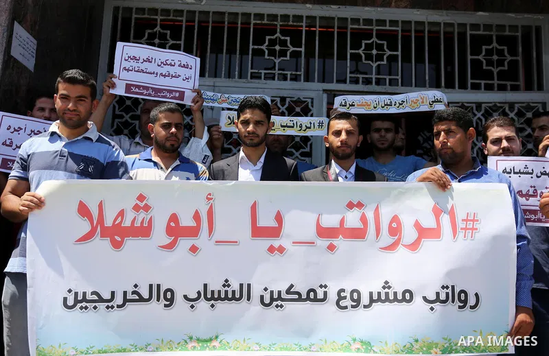 Palestinian graduates who work at temporary projects hold placards during a protest to demand their salaries, in front of Bank of Palestine in Gaza city on June 18, 2017. Photo by Ashraf Amra