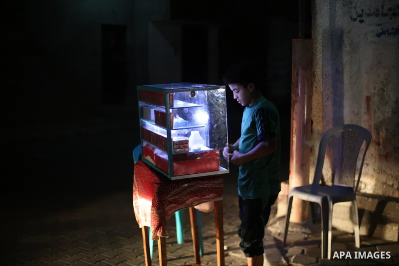 A Palestinian boy sells smoke during a power cut, outside his house at Al-Shate' refugee camp, in Gaza city on June 19, 2017. Photo by Mohammed Asad