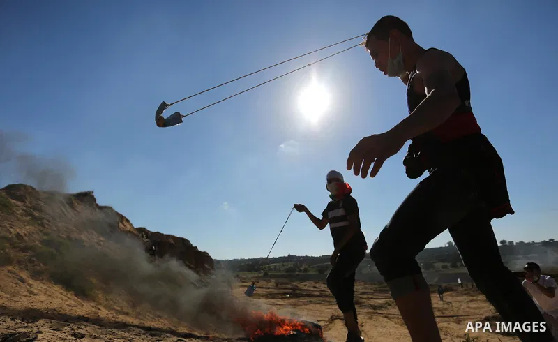 A Palestinian protester uses a slingshot to hurl stones toward Israeli security forces during clashes near the border between Israel and Central Gaza Strip east of Bureij on June 23, 2017. Photo by Ashraf Amra