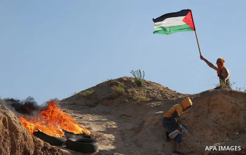 A Palestinian protester waves the national flag during clashes with Israeli security forces near the border between Israel and Central Gaza Strip of Bureij on June 23, 2017. Photo by Ashraf Amra