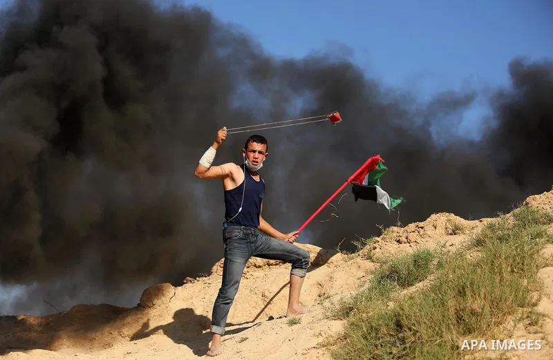 A Palestinian protester uses a slingshot to hurl stones toward Israeli security forces during clashes near the border between Israel and Central Gaza Strip east of Bureij on June 23, 2017. Photo by Ashraf Amra