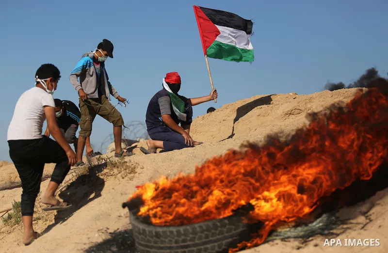 Palestinian protesters wave the national flag during clashes with Israeli security forces near the border between Israel and Central Gaza Strip of Bureij on June 23, 2017. Photo by Ashraf Amra