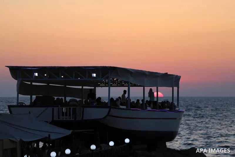 Palestinians sit in a coffee shop look like a fishing boat during the sunset on the beach of Gaza city, on June 29, 2017. Photo by Mohammed Asad