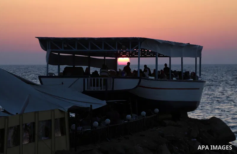 Palestinians sit in a coffee shop look like a fishing boat during the sunset on the beach of Gaza city, on June 29, 2017. Photo by Mohammed Asad