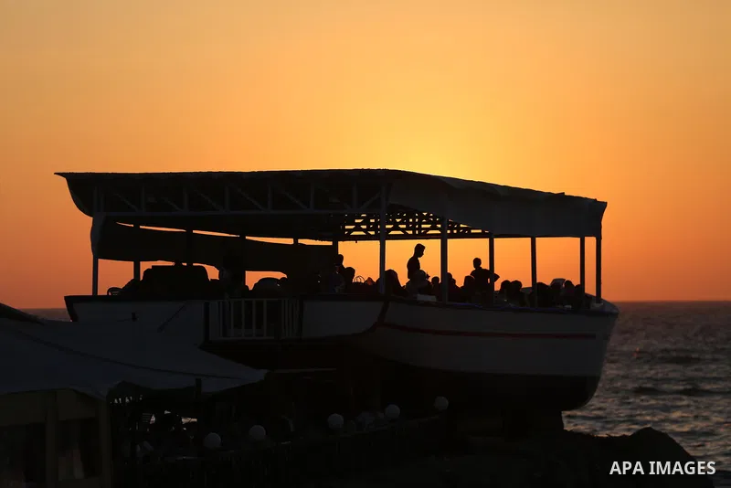Palestinians sit in a coffee shop look like a fishing boat during the sunset on the beach of Gaza city, on June 29, 2017. Photo by Mohammed Asad