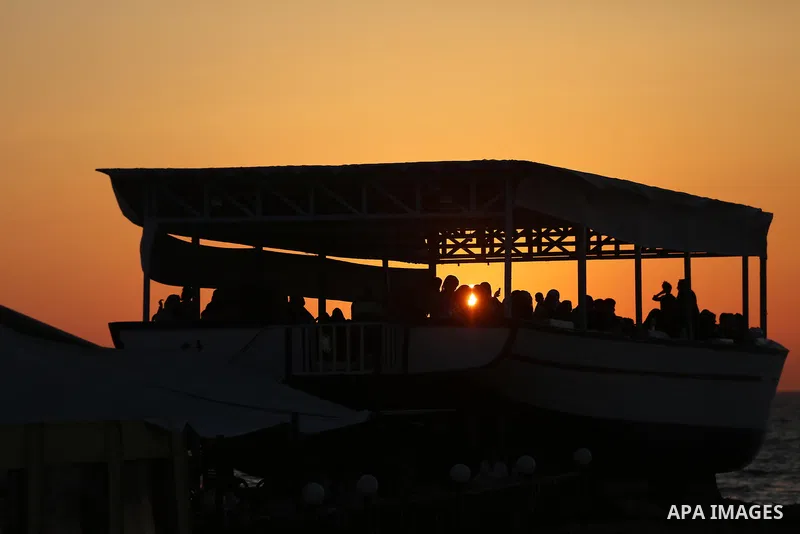 Palestinians sit in a coffee shop look like a fishing boat during the sunset on the beach of Gaza city, on June 29, 2017. Photo by Mohammed Asad