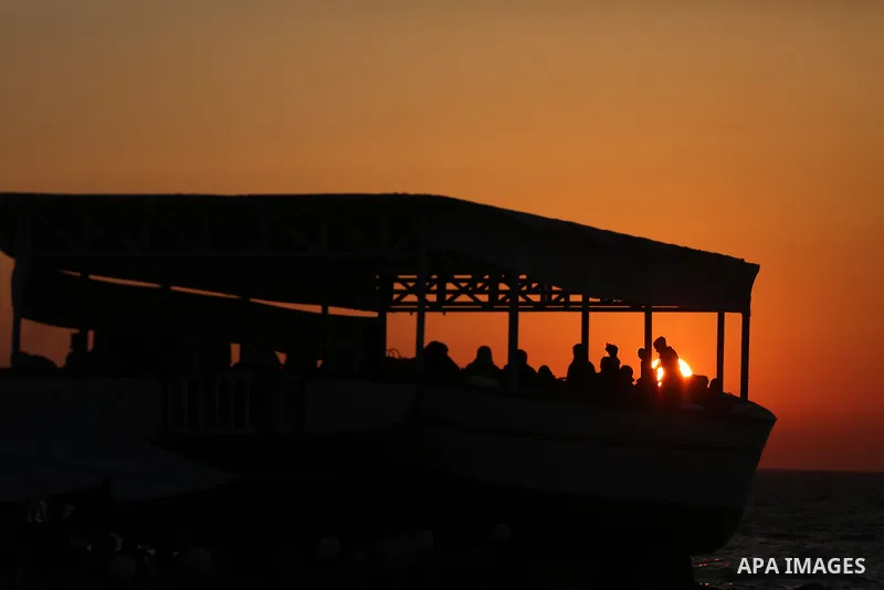 Palestinians sit in a coffee shop look like a fishing boat during the sunset on the beach of Gaza city, on June 29, 2017. Photo by Mohammed Asad