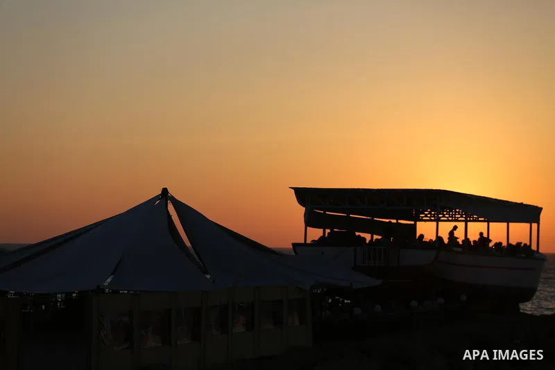 Palestinians sit in a coffee shop look like a fishing boat during the sunset on the beach of Gaza city, on June 29, 2017. Photo by Mohammed Asad