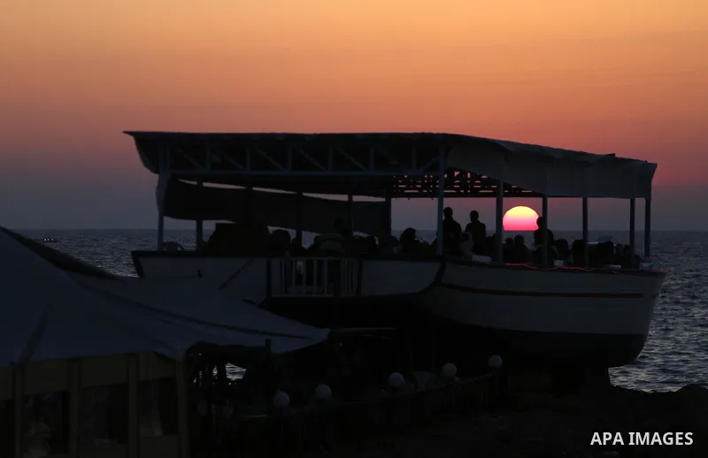 Palestinians sit in a coffee shop look like a fishing boat during the sunset on the beach of Gaza city, on June 29, 2017. Photo by Mohammed Asad