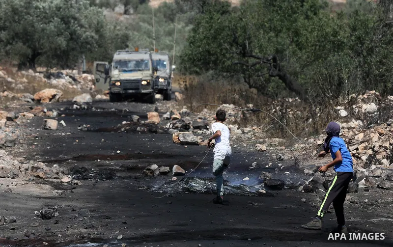 Palestinian protesters use a slingshot to hurl stones towards Israeli security forces during clashes with Palestinian protesters following a weekly demonstration against the expropriation of Palestinian land by Israel in...