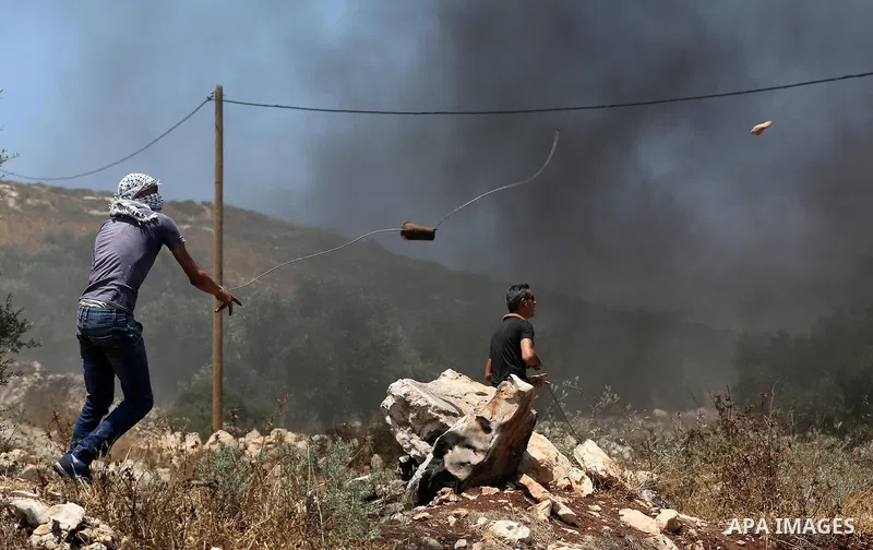A Palestinian protester uses a slingshot to hurl stones towards Israeli security forces during clashes following a weekly demonstration against the expropriation of Palestinian land by Israel in the village of Kfar Qaddu...