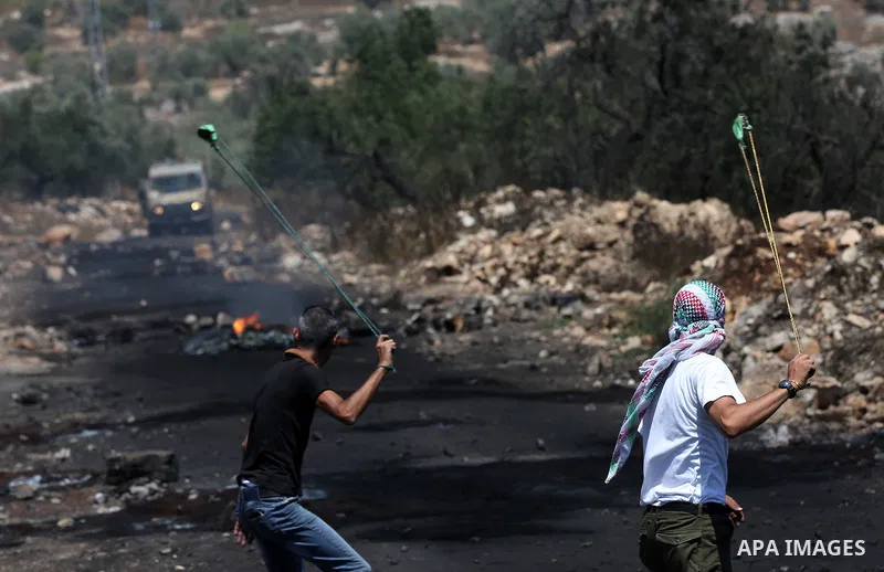 Palestinian protesters use a slingshot to hurl stones towards Israeli security forces during clashes following a weekly demonstration against the expropriation of Palestinian land by Israel in the village of Kfar Qaddum,...
