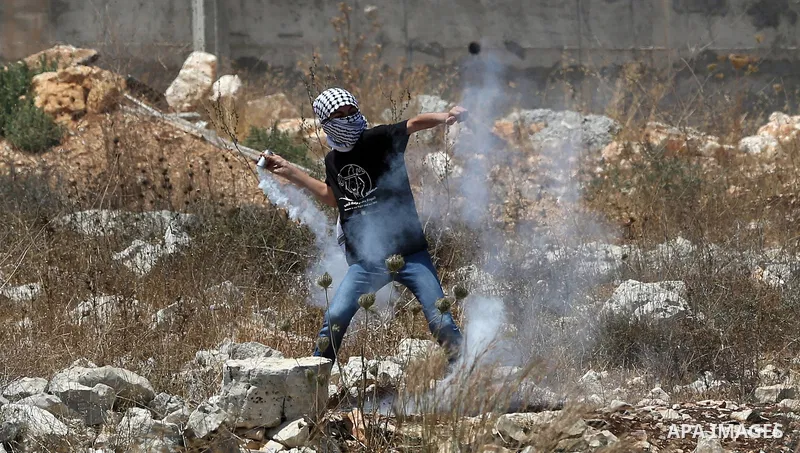 A Palestinian protester throws back a tear gas canister fired by Israeli security forces during clashes following a weekly demonstration against the expropriation of Palestinian land by Israel in the village of Kfar Qadd...