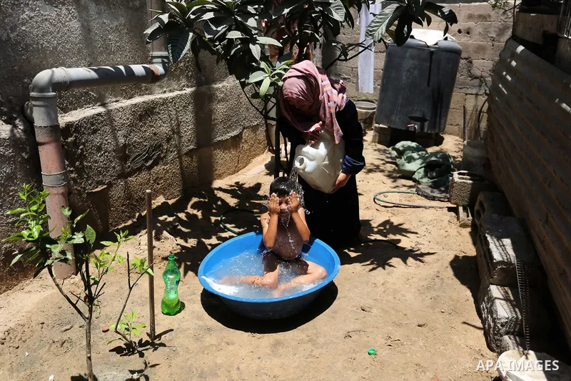 A Palestinian woman washes her son outside her house during a heatwave in Beit Lahia in the northern of Gaza Strip, on July 4, 2017. Photo by Ashraf Amra