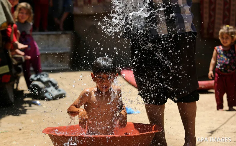 A Palestinian man washes his son outside his house during a heatwave in Beit Lahia in the northern of Gaza Strip, on July 4, 2017. Photo by Ashraf Amra
