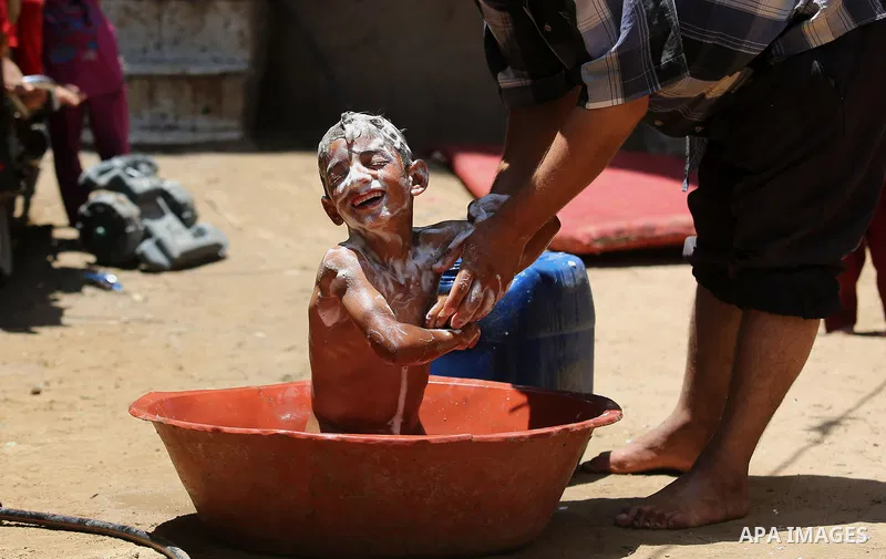 A Palestinian man washes his son outside his house during a heatwave in Beit Lahia in the northern of Gaza Strip, on July 4, 2017. Photo by Ashraf Amra