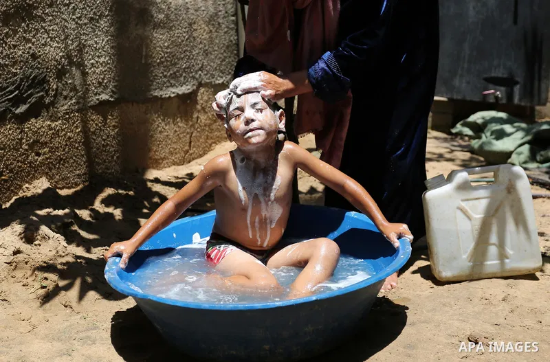 A Palestinian woman washes her son outside her house during a heatwave in Beit Lahia in the northern of Gaza Strip, on July 4, 2017. Photo by Ashraf Amra