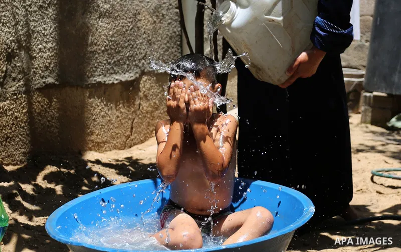 A Palestinian woman washes her son outside her house during a heatwave in Beit Lahia in the northern of Gaza Strip, on July 4, 2017. Photo by Ashraf Amra