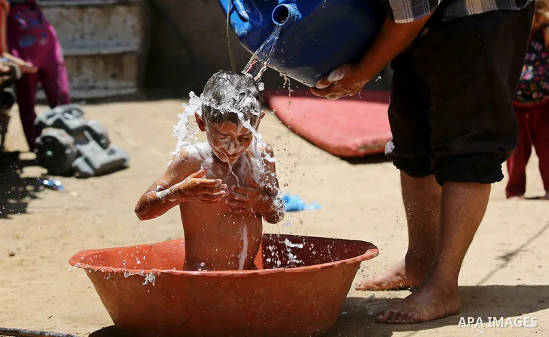 A Palestinian man washes his son outside his house during a heatwave in Beit Lahia in the northern of Gaza Strip, on July 4, 2017. Photo by Ashraf Amra