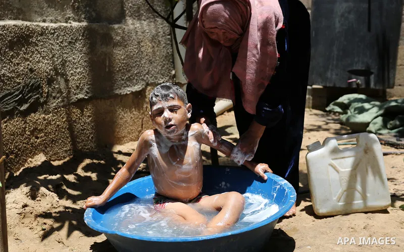 A Palestinian woman washes her son outside her house during a heatwave in Beit Lahia in the northern of Gaza Strip, on July 4, 2017. Photo by Ashraf Amra
