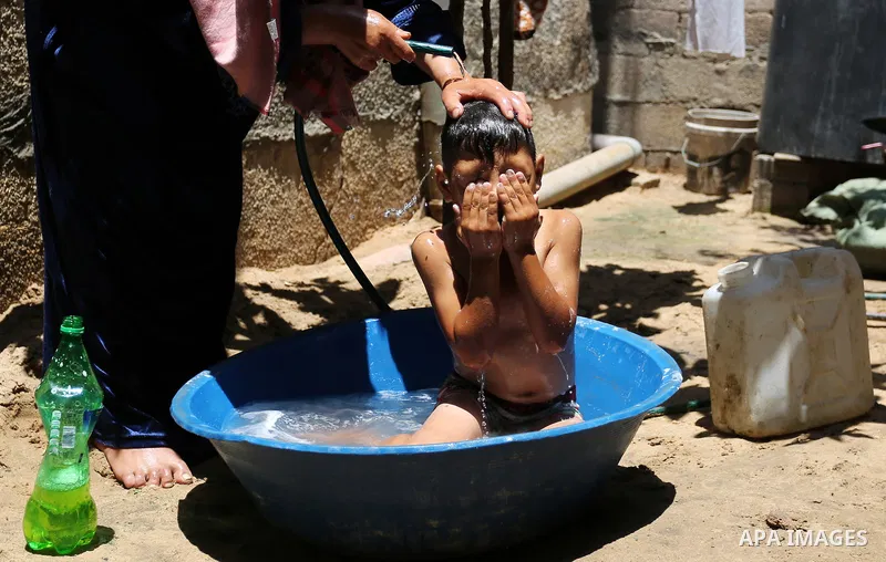 A Palestinian woman washes her son outside her house during a heatwave in Beit Lahia in the northern of Gaza Strip, on July 4, 2017. Photo by Ashraf Amra