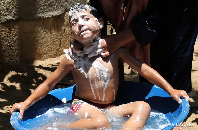 A Palestinian woman washes her son outside her house during a heatwave in Beit Lahia in the northern of Gaza Strip, on July 4, 2017. Photo by Ashraf Amra