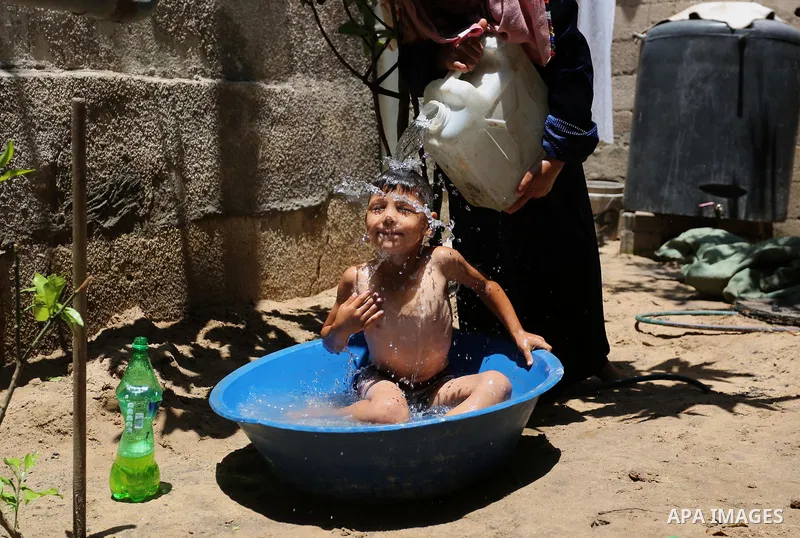A Palestinian woman washes her son outside her house during a heatwave in Beit Lahia in the northern of Gaza Strip, on July 4, 2017. Photo by Ashraf Amra