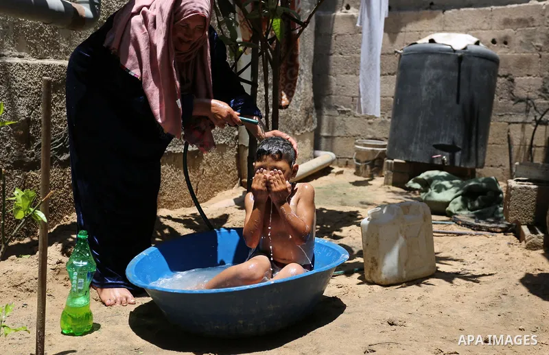 A Palestinian woman washes her son outside her house during a heatwave in Beit Lahia in the northern of Gaza Strip, on July 4, 2017. Photo by Ashraf Amra