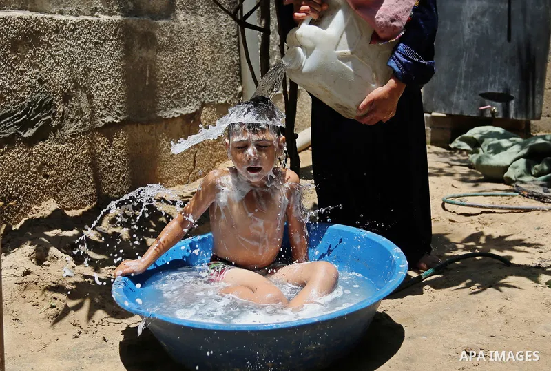 A Palestinian woman washes her son outside her house during a heatwave in Beit Lahia in the northern of Gaza Strip, on July 4, 2017. Photo by Ashraf Amra