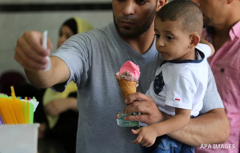 A Palestinian man holds his son as he buys ice-cream (sundae) during a heatwave in Gaza city on July 4, 2017. Photo by Ashraf Amra