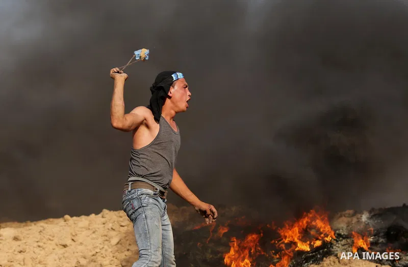 A Palestinian protester uses a slingshot to hurl stones towards Israeli security forces during clashes near the border between Israel and Central Gaza Strip July 7, 2017. Photo by Ashraf Amra