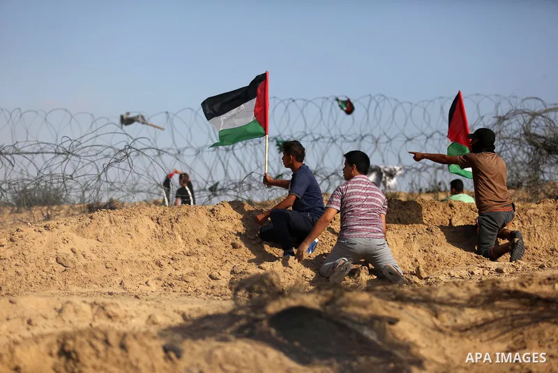 Palestinian protesters wave the national flag during clashes with Israeli security forces near the border between Israel and Central Gaza Strip July 7, 2017. Photo by Ashraf Amra