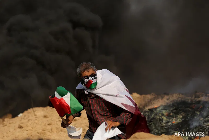 A Palestinian protester wears a Qatar flag and waves the national flag during clashes with Israeli security forces near the border between Israel and Central Gaza Strip July 7, 2017. Photo by Ashraf Amra